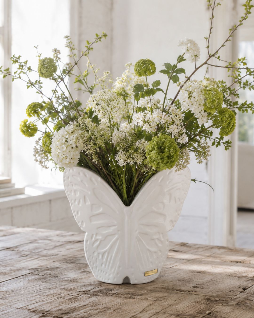 Carolina Gynning vit fjärilsvas fylld med vita och gröna sommarblommor på träbord i ljus lantlig miljö.